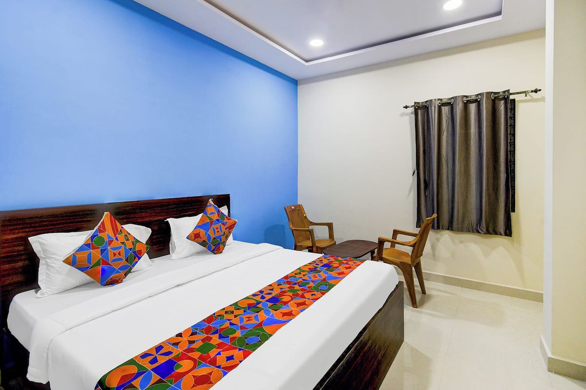 Habitación de hotel con cama, una mesita pequeña, dos sillas, ventana con cortinas y una lámpara en el techo.
