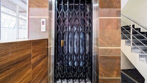 An elevator with a metal grille door, a control panel with a red 'G' button, and a staircase with black steps to the right. - Fabhotel Golden City Inn (Hyderabad)