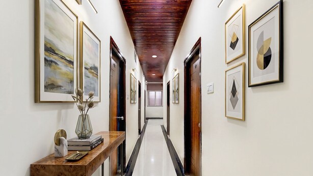 A hallway with framed artwork on the walls, a wooden console table with books and a vase, and a polished floor. - Fabhotel Golden City Inn (Hyderabad)