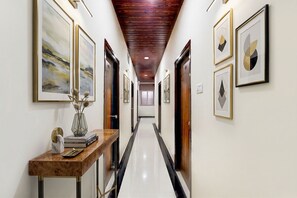 A hallway with framed artwork on the walls, a wooden console table with books and a vase, and a polished floor. - FabHotel Golden City Inn - ECIL X Roads, ECIL (Hyderabad)