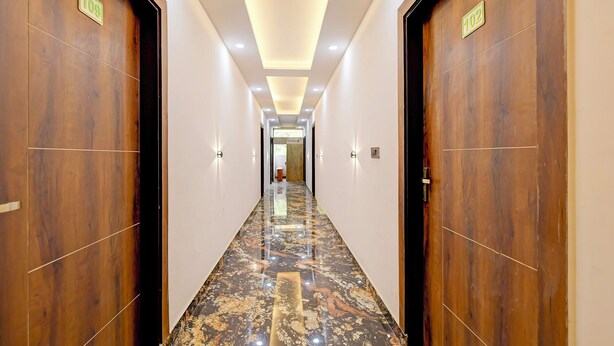 Passadís d'hotel amb portes de fusta, indicadors de números de habitació i un paviment de marbre.