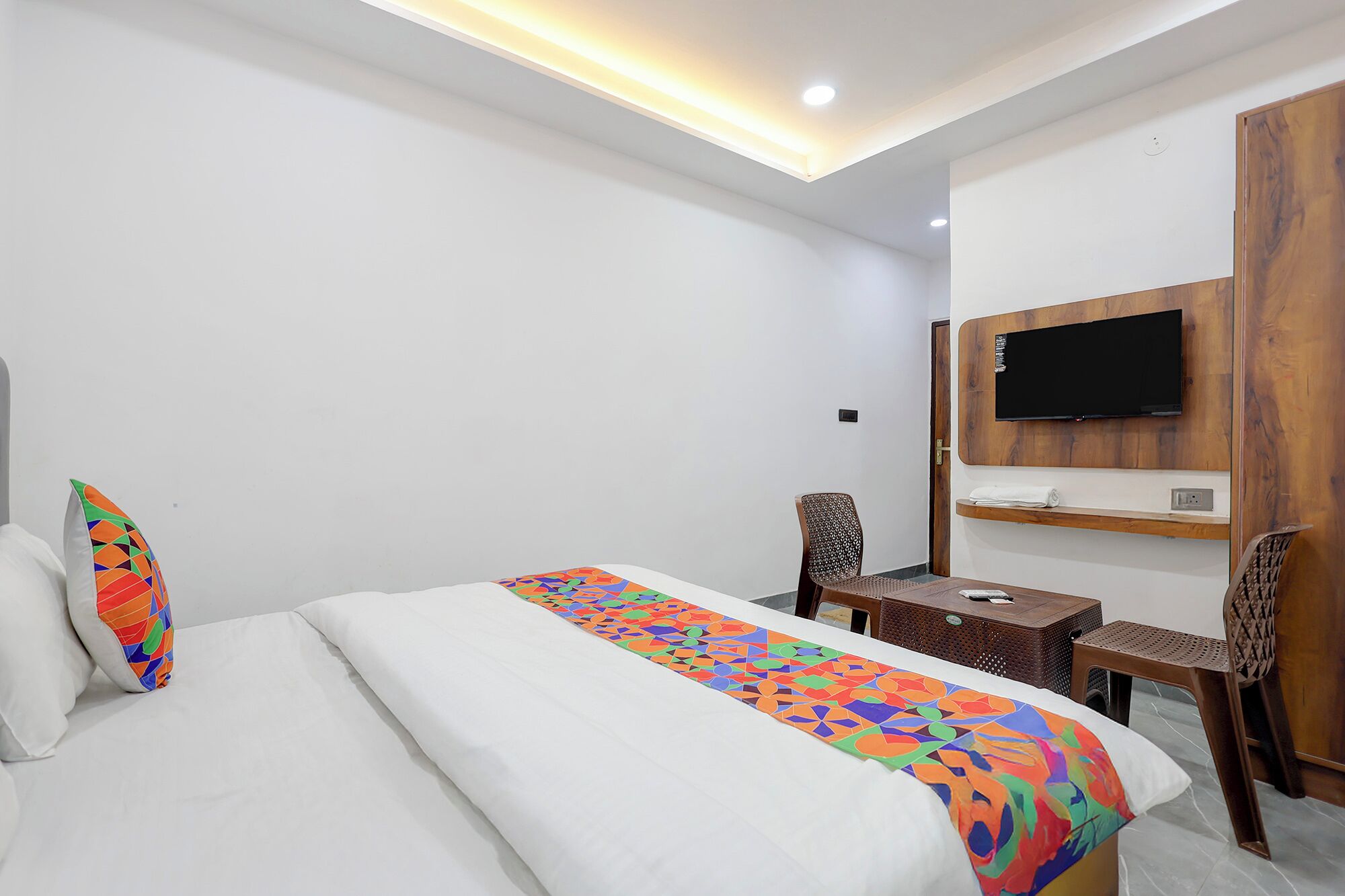 A hotel room with a bed, a desk, a TV mounted on a wooden panel, and a chair.