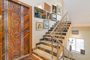 A staircase with a railing, a wooden door with a patterned design, and several framed pictures on the walls. - Via Safehome Guest House (Barasat)