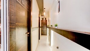 A hallway with a wooden door labeled 'G1', a white wall with a framed picture, and a potted plant on a ledge. - Fabhotel Nm (Mumbai)