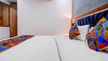 A hotel room with a bed, a wooden wardrobe, and a wall-mounted air conditioner.
