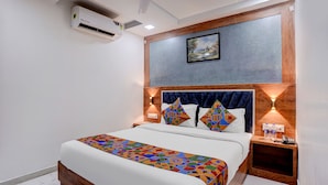 A bedroom with a bed, a headboard, a wall-mounted air conditioner, a framed picture, and bedside lamps. - Fabhotel Nm (Mumbai)