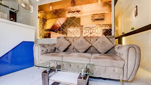 A living room with a beige sofa, a glass coffee table, and a view of a staircase and balcony. - Fabhotel Nm (Mumbai)