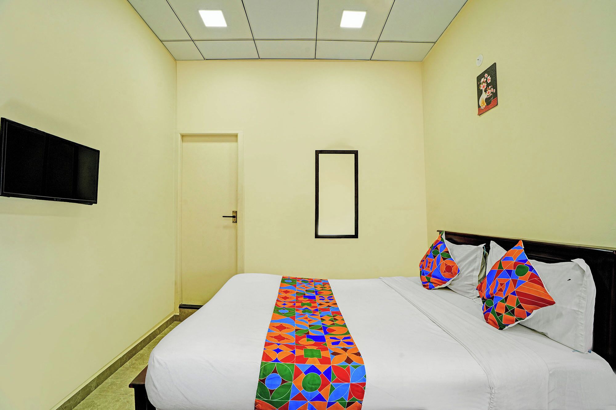 A hotel room with a bed, a television mounted on the wall, and a door.