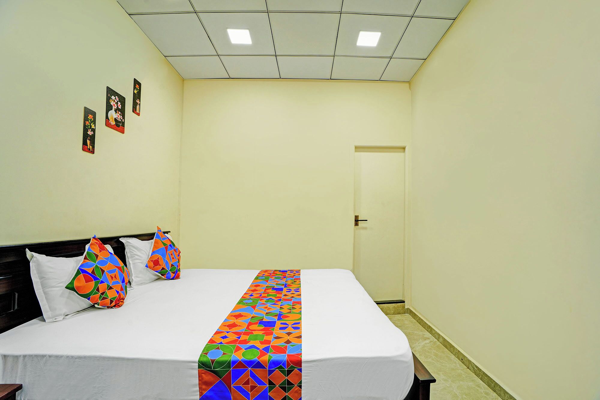 A hotel room with a bed, a door, and a wall with three framed pictures.