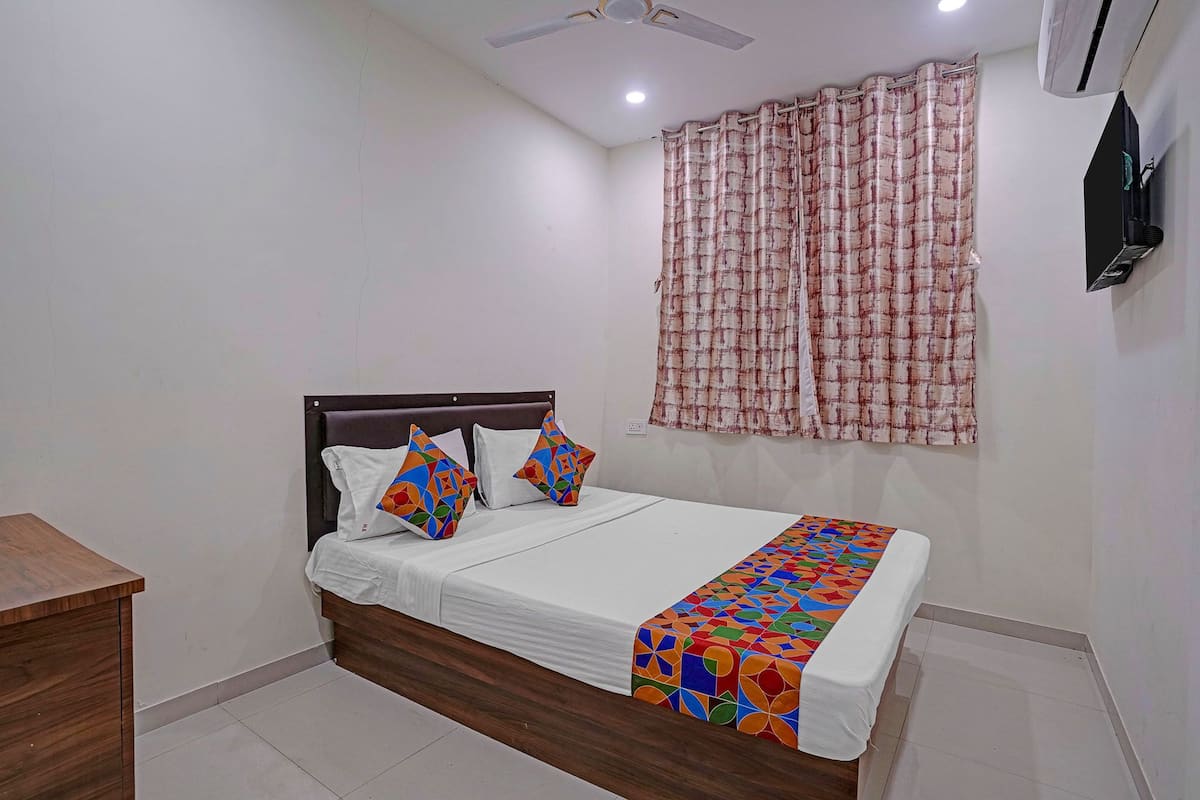 A bedroom with a bed, pillows, a bedside table, a window with curtains, and a ceiling fan.