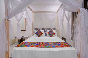 Een bed met hemel, nachtkastje en spiegel.