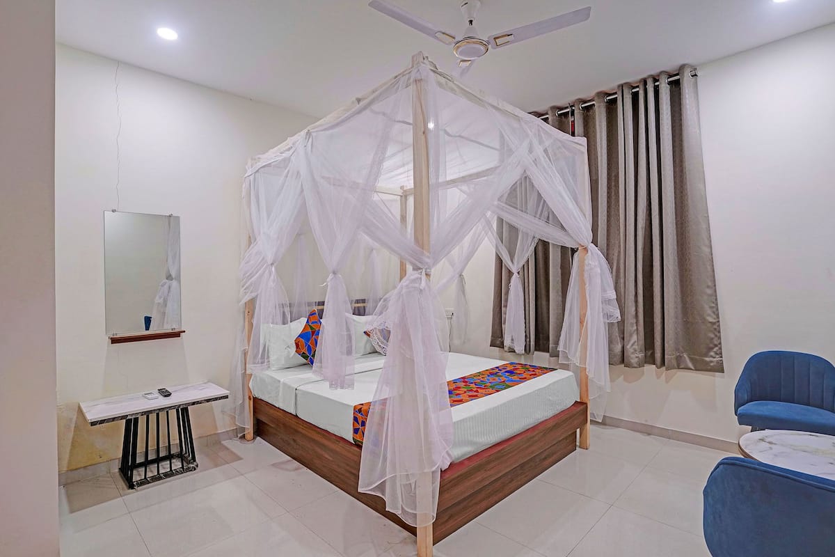 A bedroom with a four-poster canopy bed, a bedside table, a chair, and a ceiling fan.