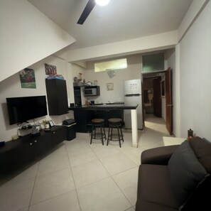 A compact living space with a kitchenette, a flat-screen TV, a sofa, and a dining area with stools. - Apartment C (Zona Romantica) (Puerto Vallarta)