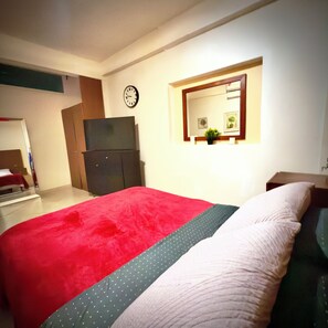 Une chambre à coucher avec un lit, une commode, une horloge et une petite fenêtre agrémentée d’une plante.