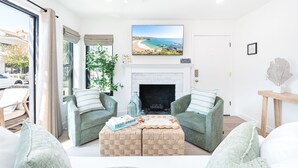 Un salon avec deux fauteuils verts, une cheminée et une grande fenêtre donnant sur une plage.