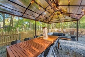 Un espace extérieur abrité, avec une table et des chaises en bois, entouré d’une clôture en bois et d’arbres.