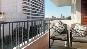 Ein Balkon mit Blick auf ein Hochhaus, einem Geländer und zwei Stühlen mit gemusterten Kissen.