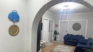 Ein Wohnzimmer mit einem blauen Sofa, einem Fernseher, einem Spiegel und einem Wandbild.