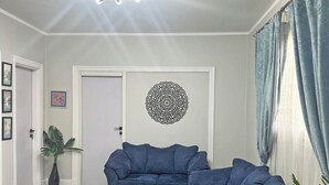 Ein Wohnzimmer mit Ecksofa, einem gemusterten Teppich, einer Wanddekoration und einem Blumentopf.