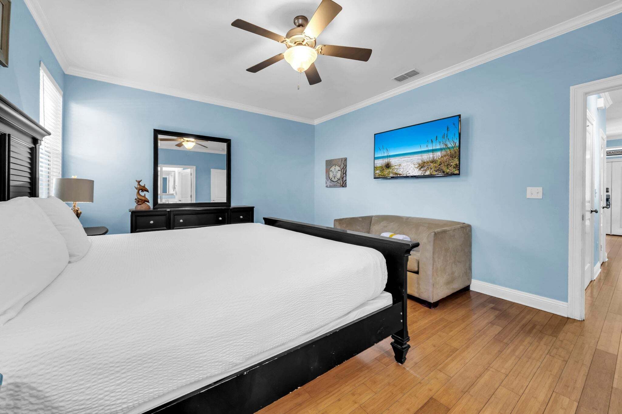 Een slaapkamer met een bed, een plafondventilator, een dressoir, een stoel en een schilderij aan de muur.