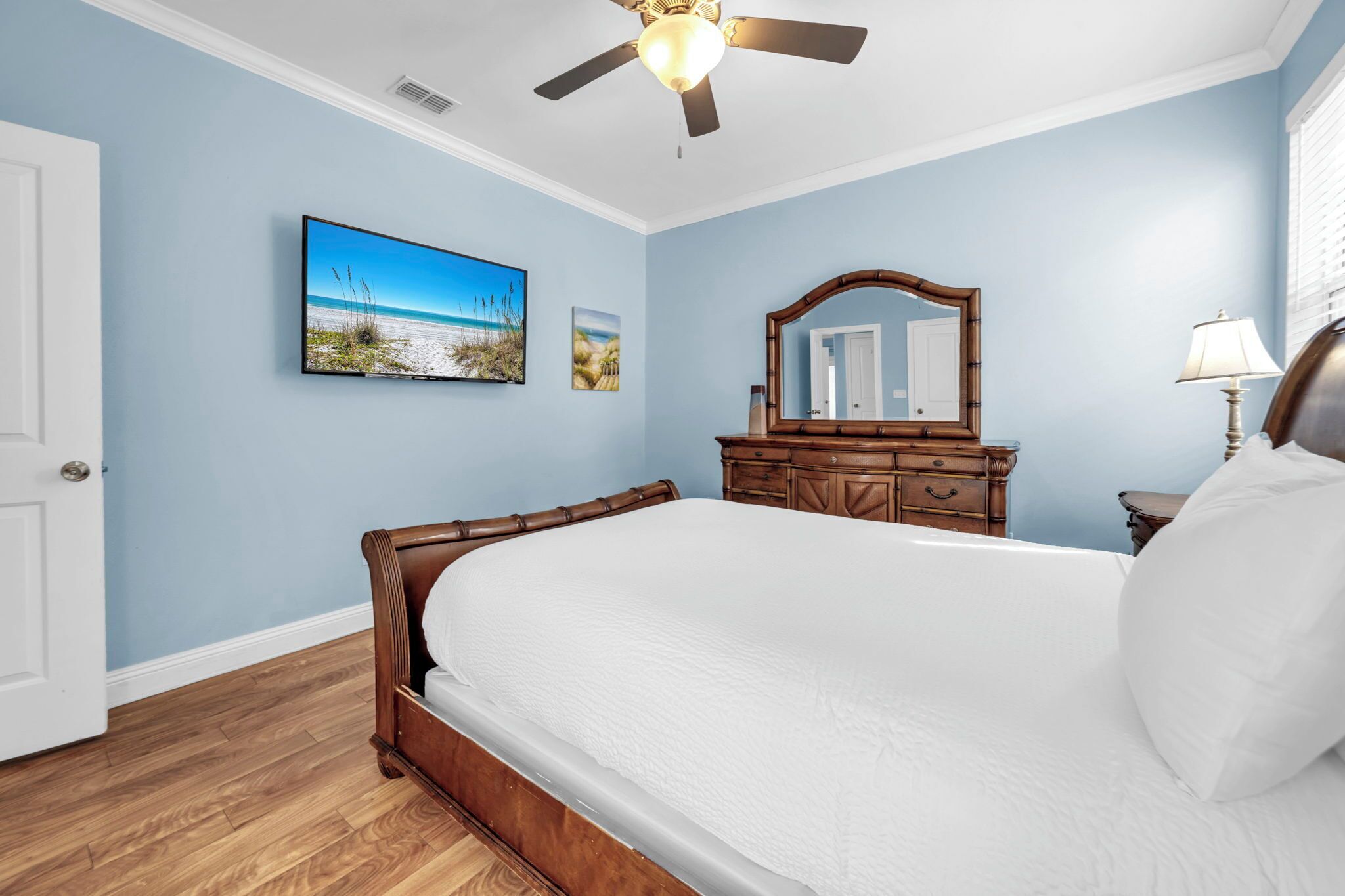 Un dormitorio con cama, ventilador de techo, cómoda de madera, espejo y televisor montado en la pared.