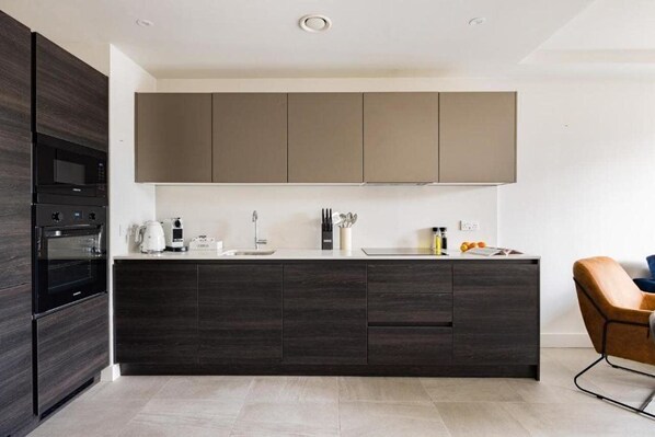 A modern kitchen with dark cabinetry, a built-in oven, and a coffee maker. - Charles Hope Leeds (Leeds)
