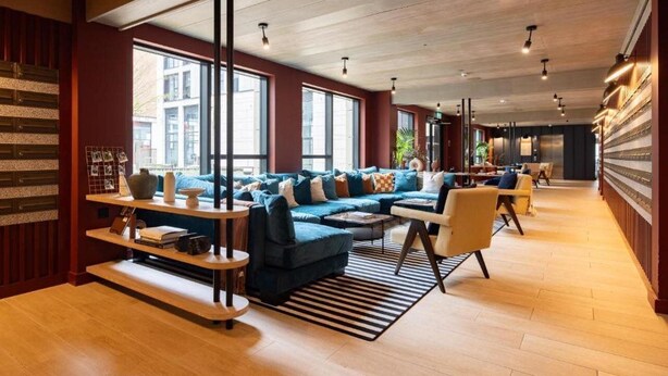 Un intérieur moderne avec un canapé d’angle bleu, un plancher en bois et de grandes fenêtres.