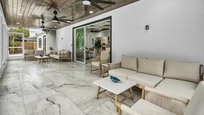 Eine geräumige Terrasse mit Marmorboden, einer Couch, Sesseln und einem Deckenventilator.