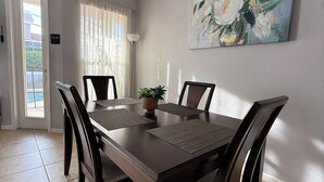 Ein Essbereich mit Holztisch und Stühlen, einem Blumentopf, einem Bild an der Wand und einer zur Außenseite führenden Tür.