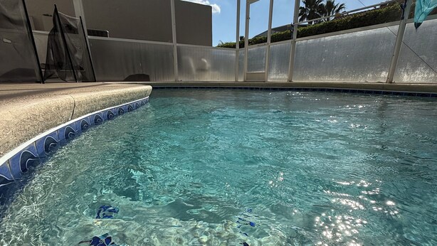 Ein heller, überdachter Schwimmbereich mit geometrischer Dachkonstruktion, klarem Wasser und einer gefliesten Kante.