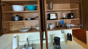 Uma cozinha com prateleiras de madeira, cafeteira e porta-facas.