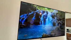 Televisão de tela plana na parede exibindo uma cena de cachoeira.