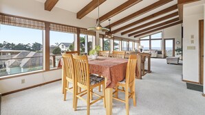 Un comedor espacioso con una mesa grande y sillas, ventanas amplias que ofrecen vistas del barrio circundante y un techo alto con vigas de madera a la vista.