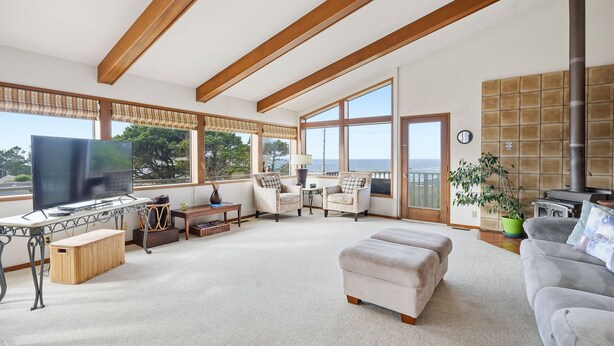 Un salón amplio con televisor grande, vigas de madera, chimenea y un balcón con vistas.