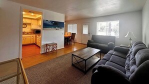 A living room with a sofa, a coffee table, a dining area with a table and chairs, and a kitchen visible through an open doorway. - Spacious 3BR Desert Condo | Pools, Tennis & Near El Paseo Shopping (Palm Desert)