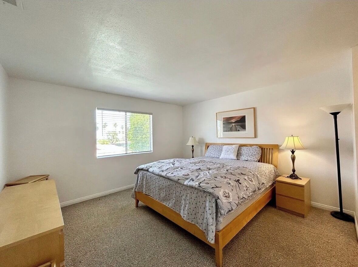 A bedroom with a bed, nightstands, a lamp, a window, and a framed picture on the wall.