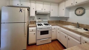 A kitchen with white cabinets, a stove, a refrigerator, and a clock on the wall. - Spacious 3BR Desert Condo | Pools, Tennis & Near El Paseo Shopping (Palm Desert)