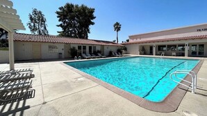 A swimming pool with lounge chairs, a covered area, and a building with a tiled roof. - Spacious 3BR Desert Condo | Pools, Tennis & Near El Paseo Shopping (Palm Desert)