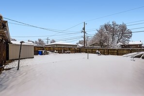 A snow-covered backyard with a wooden fence, a utility shed, and a tree. - Charming 3-bedroom house in Denver, Quiet with Yard and Easy Commute (Denver)