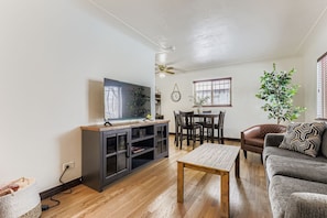 Ein Wohnzimmer mit Flachbildfernseher, Holzboden, einer Couch, einem Couchtisch und einem Essbereich mit Stühlen.