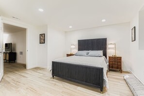 Ein Schlafzimmer mit einem Bett, Nachttischen, einer Kommode und einer Tür zu einem anderen Raum.
