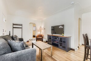 Ein Wohnzimmer mit einer Couch, einem Holztisch, einem Fernseher auf einem Schrank und einem Sessel.