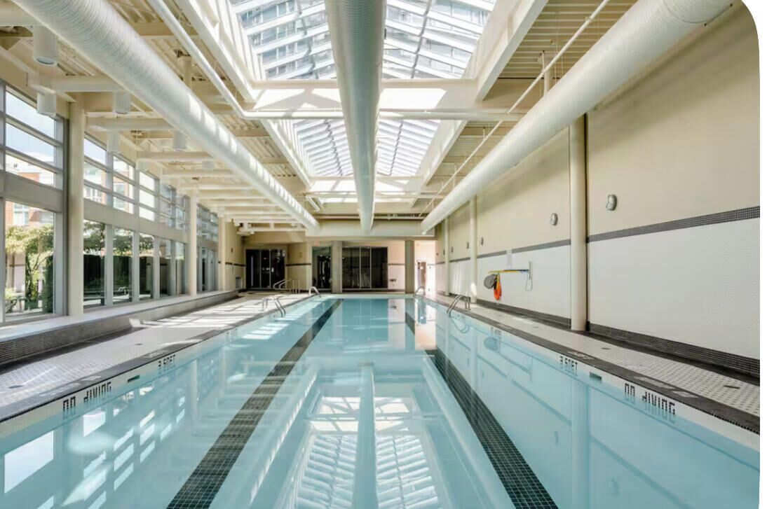 A swimming pool with clear glass walls, a skylight ceiling, and a tiled floor.