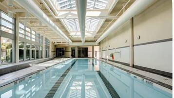A swimming pool with clear glass walls, a skylight ceiling, and a tiled floor.