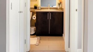 A narrow hallway leading to a bathroom with a dark cabinet, a sink, and a mirror. - Vancouver downtown apartment (Vancouver)