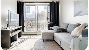 A modern living room with a flat-screen TV, a sofa, a coffee table, and a large window with curtains. - Vancouver downtown apartment (Vancouver)