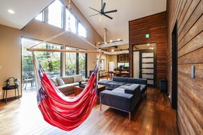 Een ruime woonruimte met een hangmat, modern meubilair, grote ramen en een houten wand.