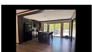 A modern kitchen with dark cabinetry, a central island, and a dining area with chairs. - Beachfront private rental on Lake Eufaula- sleeps 7 guest and pet-friendly (Longtown)
