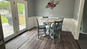 Un comedor con una mesa redonda, cuatro sillas, un adorno en la pared y un ventanal corredizo que da a una terraza exterior.