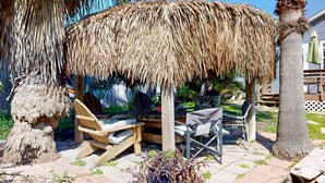Un espacio de estar al aire libre con techo de paja, mobiliario de madera y una palmera.